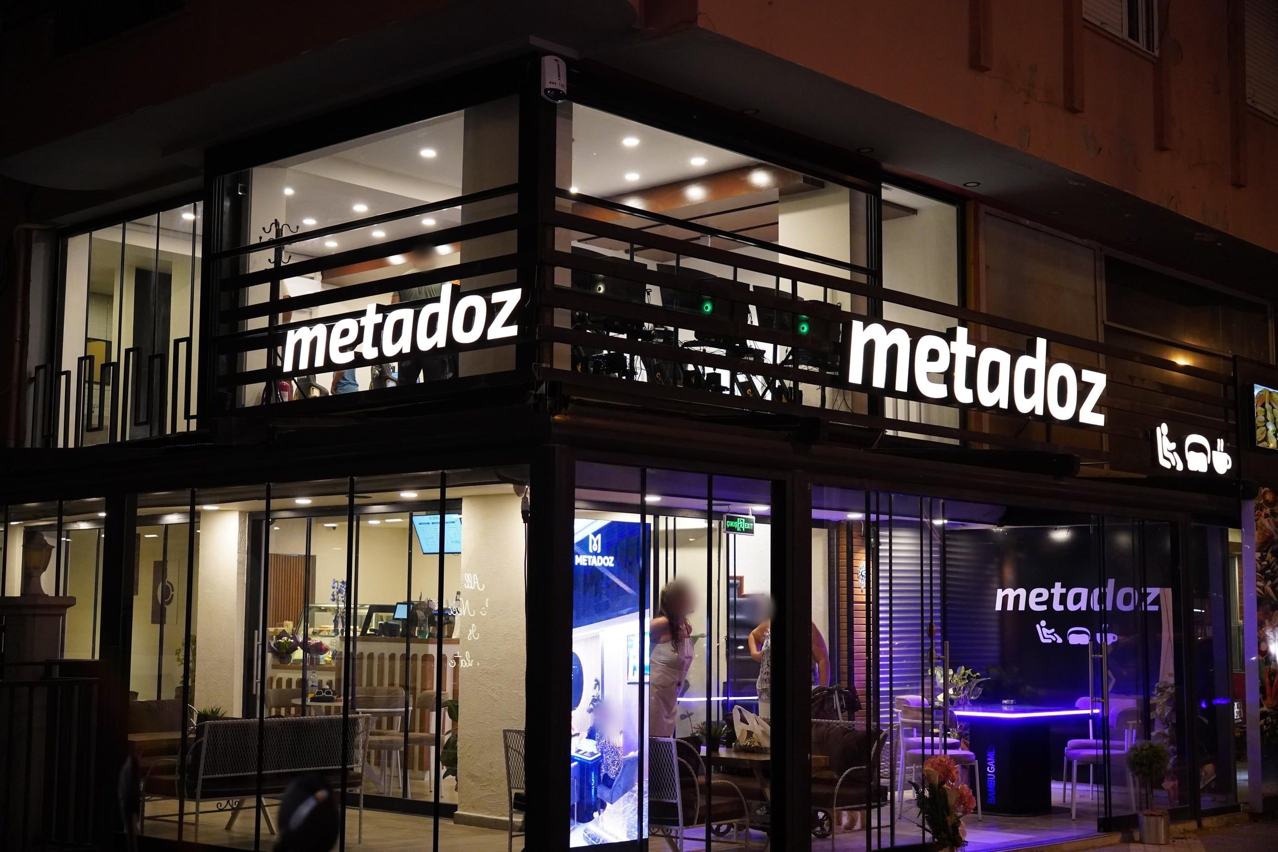 Metadoz'un ışıklı tabelaları ve cam cephesinin gece görünümü.
