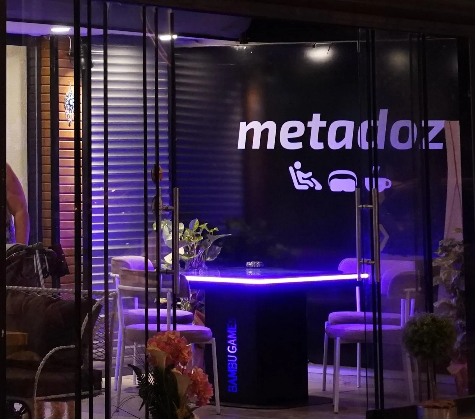 Metadoz'un zemin katı: mor ışıklı masa, oturma alanı ve simgeli Metadoz tabelası, cam cepheden görünüm.